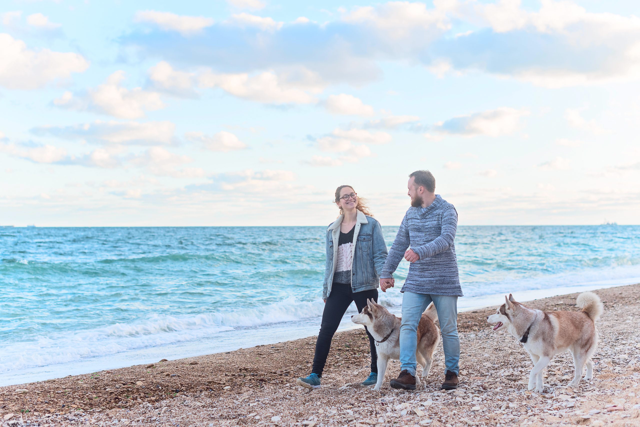 Couple lovers smiling, hold hands and walking along the coast with husky dogs